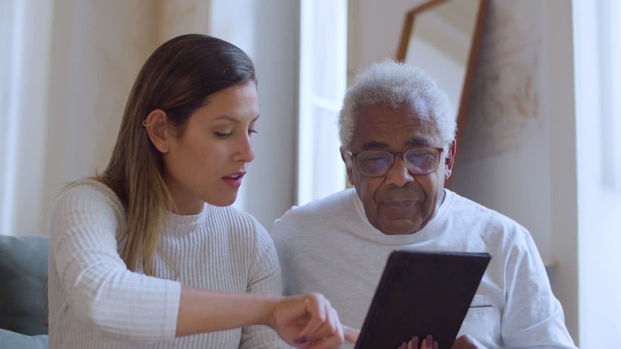 Young Caucasian girl helping her grandpa with using tablet.