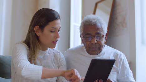 young caucasian girl helping her grandpa with using tablet.