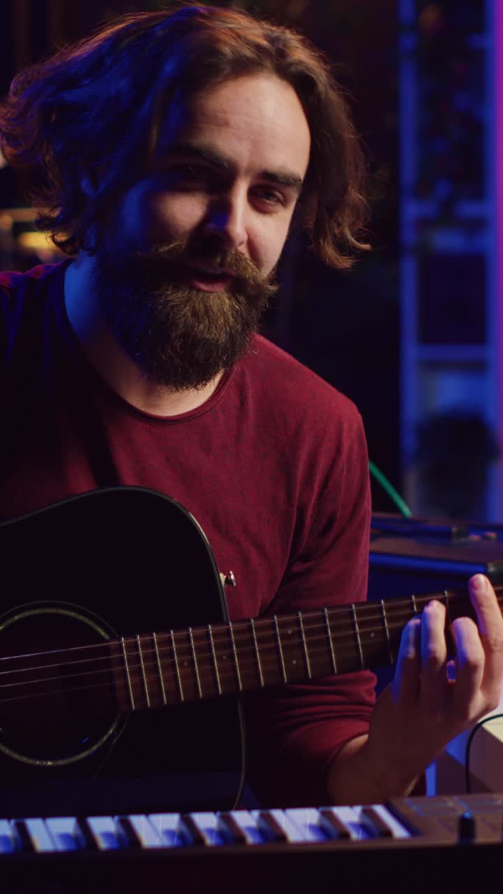 Hombre barbudo tocando la guitarra acústica y hablando en un estudio en casa
