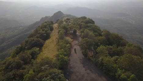 aerial: motorcycle rider approaches mountain viewpoint in rural india