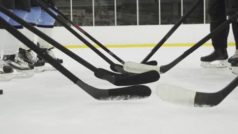 bei einem eishockey-wettbewerb stellen die spieler ihre hockeyschläger in eine reihe und stoßen damit sanft auf das eis