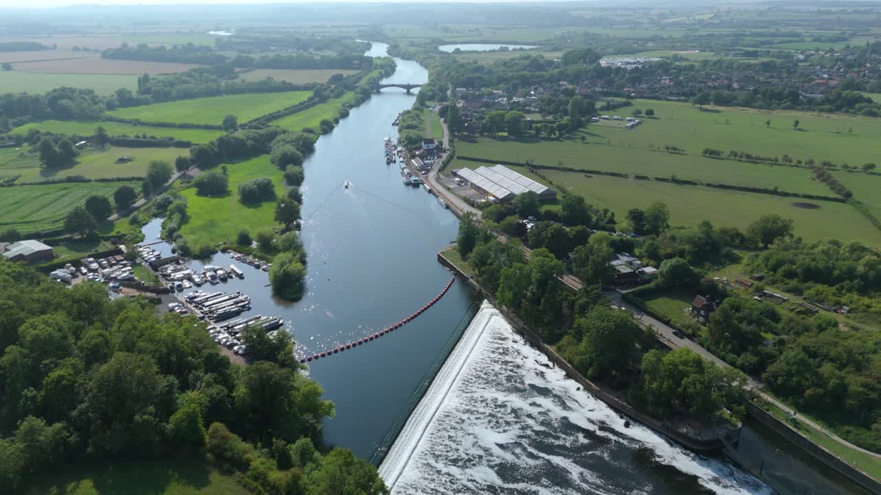 Aerial panning drone shot of canal boat on River Trent England with green rural countryside landscape fields and summer evening golden light scenery