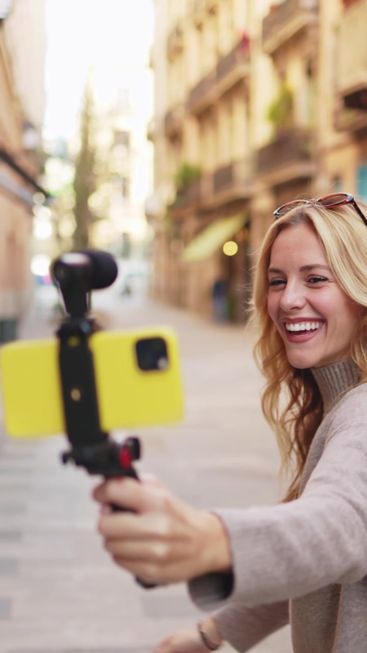 Giovane donna felice che fa vlogging per strada in città con lo smartphone