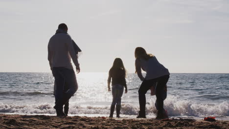 rear view of family jumping over waves looking out to sea silhouetted against sun