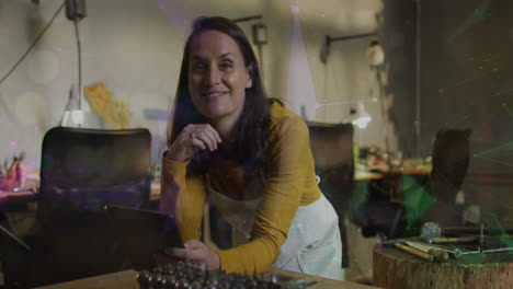 animation of spots of light over caucasian woman wearing an apron using digital tablet at workshop