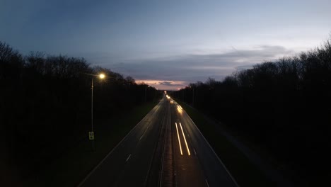 long highway traffic streak lights into distant sunrise horizon