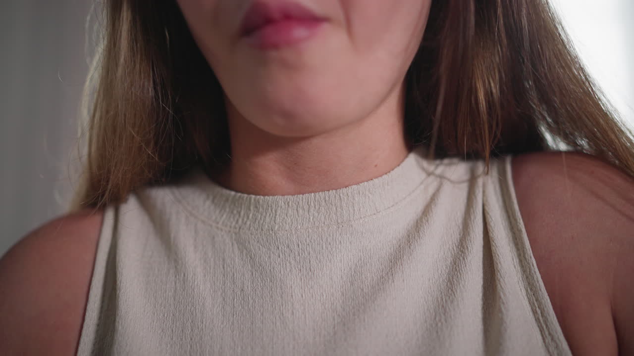 Close up of girl gently chewing with jaw moving while eating with chopstick, textured cream sleeveless top visible, long brown hair cascading behind shoulders