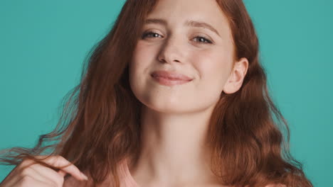 redheaded girl in front of camera on turquoise background.