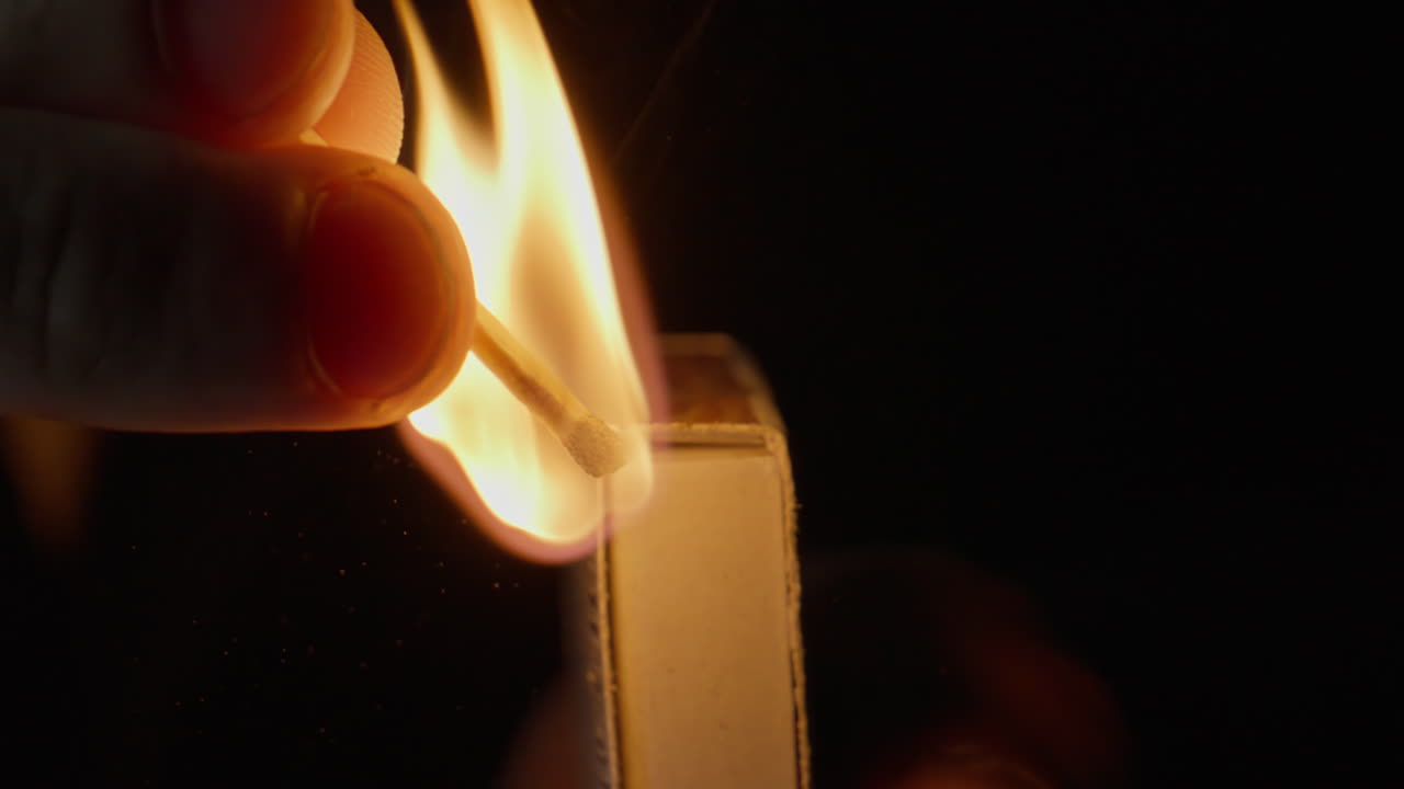 Fingers holding burnt matchstick near box slowly fading glowing fire closeup