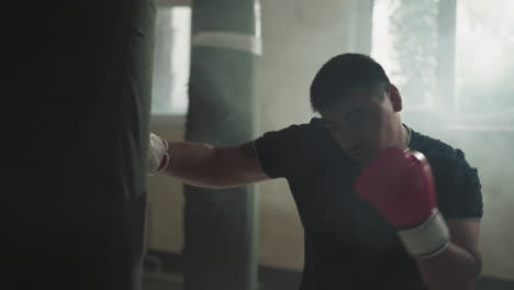 man punches heavy bag with hooks in sports club. professional sportsman has active training in equipped gym with dust cloud slow motion. martial arts exercises