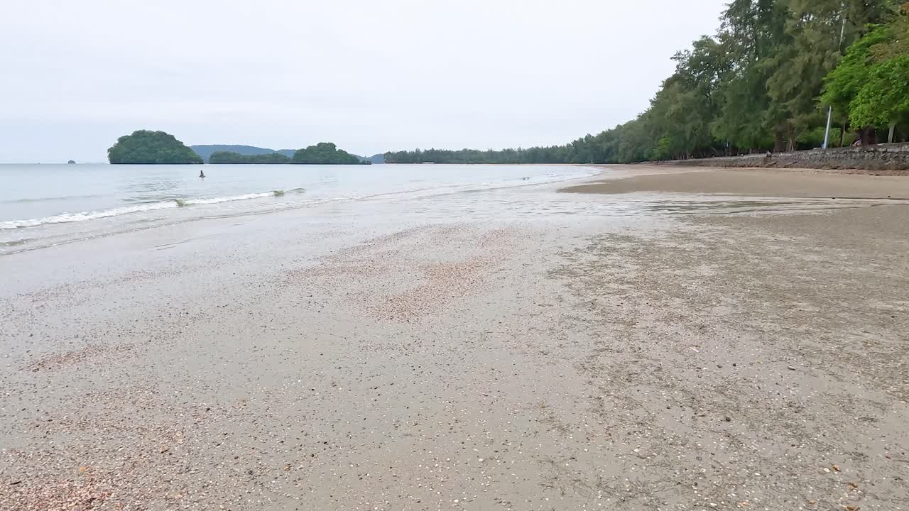 태국 크라비의 조용한 해변 풍경, 부드러운 파도, 모래 해변, 부드런 낮빛 아래 울창한 초록색을 보여줍니다.