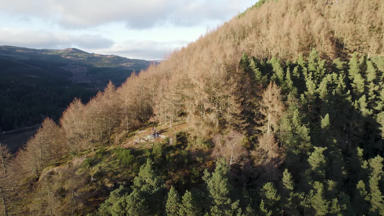 imágenes aéreas de drones que se elevan sobre un acantilado que revelan personas mirando desde un peñasco de montaña cubierto de bosque, un valle, pinos silvestres y alerces