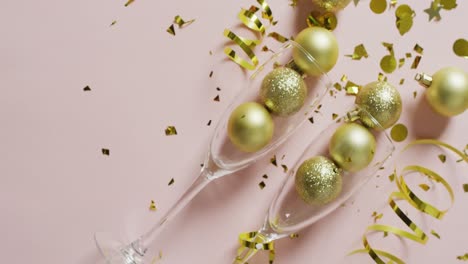 Video-of-gold-baubles-in-two-champagne-glasses-with-streamers-and-confetti-on-white,-with-copy-space