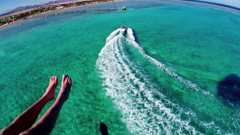 Parasailing-point-of-view-couple-feet-above-blue-turquoise-ocean-waters-flying,-water-sports-in-slow-motion-perspective