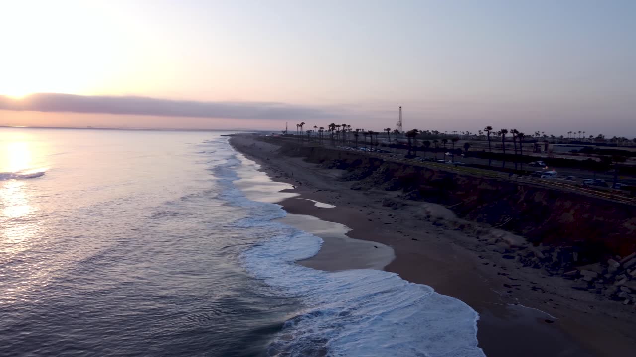 Molo di Huntington Beach sulla Pacific Coast Highway 1. Auto che passano accanto a palme tropicali al tramonto. Calda luce dorata e onde tranquille dell'oceano. Orange County, California