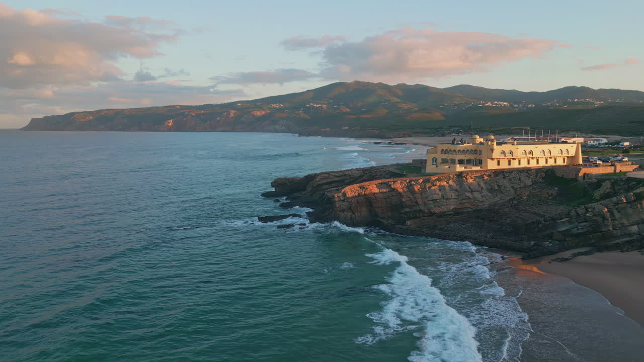 Aerial sunrise coastline awakening with warm morning light on cliffs beach.