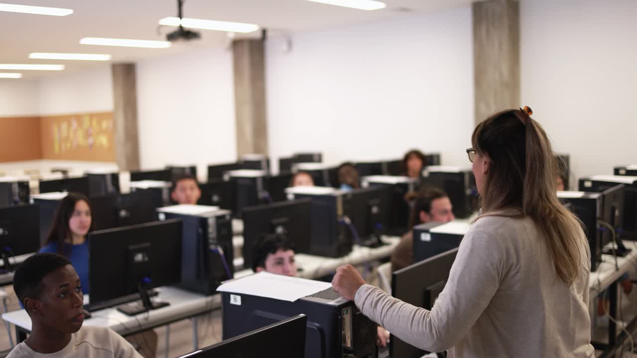 maestra madura trabajando con estudiantes multirraciales dentro de la sala de computadoras de la universidad