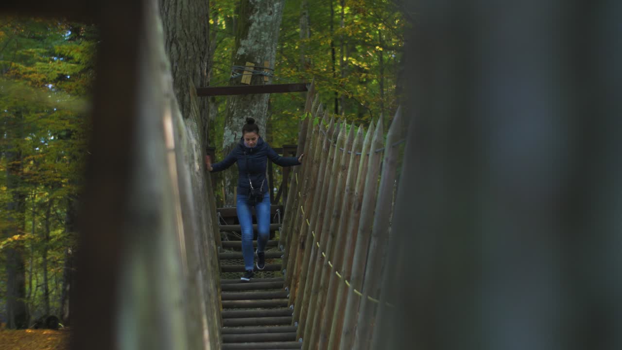 девушка перебирается через веревочный мост в солнечный осенний день