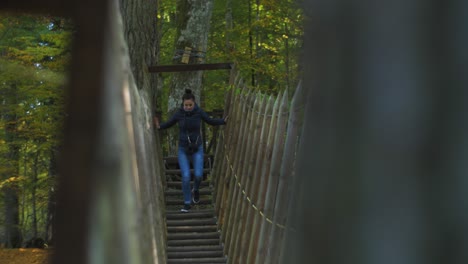 girl climbs over the rope bridge in sunny autumn day