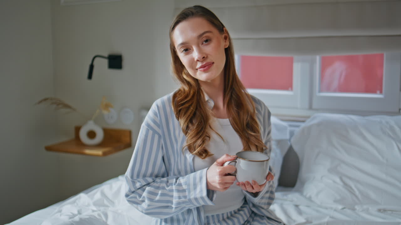 Relaxed lady holding cup beverage on comfortable bed at weekend morning closeup