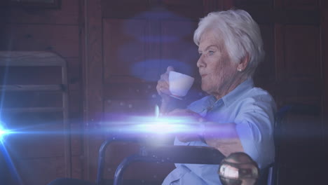 animation of light moving over smiling senior caucasian woman in wheelchair drinking tea