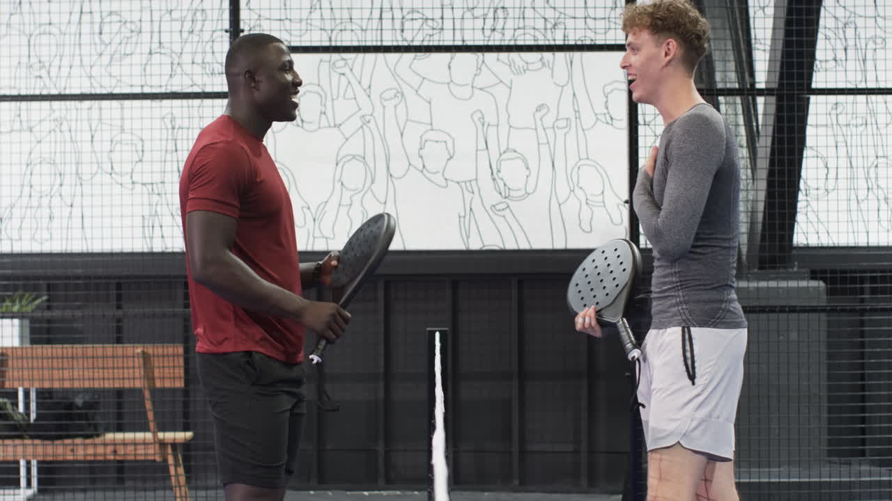 Two diverse men playing padel tennis indoors, enjoying game and competition, at indoor court