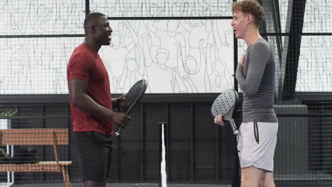 two diverse men playing padel tennis indoors, enjoying game and competition, at indoor court