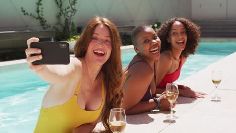 grupo diverso de amigas divirtiéndose en la piscina tomando selfies