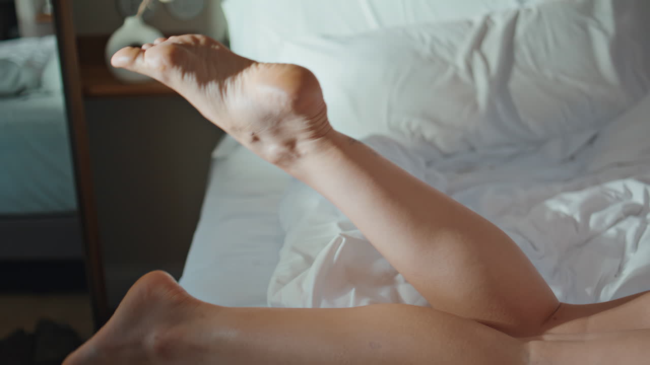 Closeup legs lying bed in morning sunlight. Resting woman enjoy leisure at home