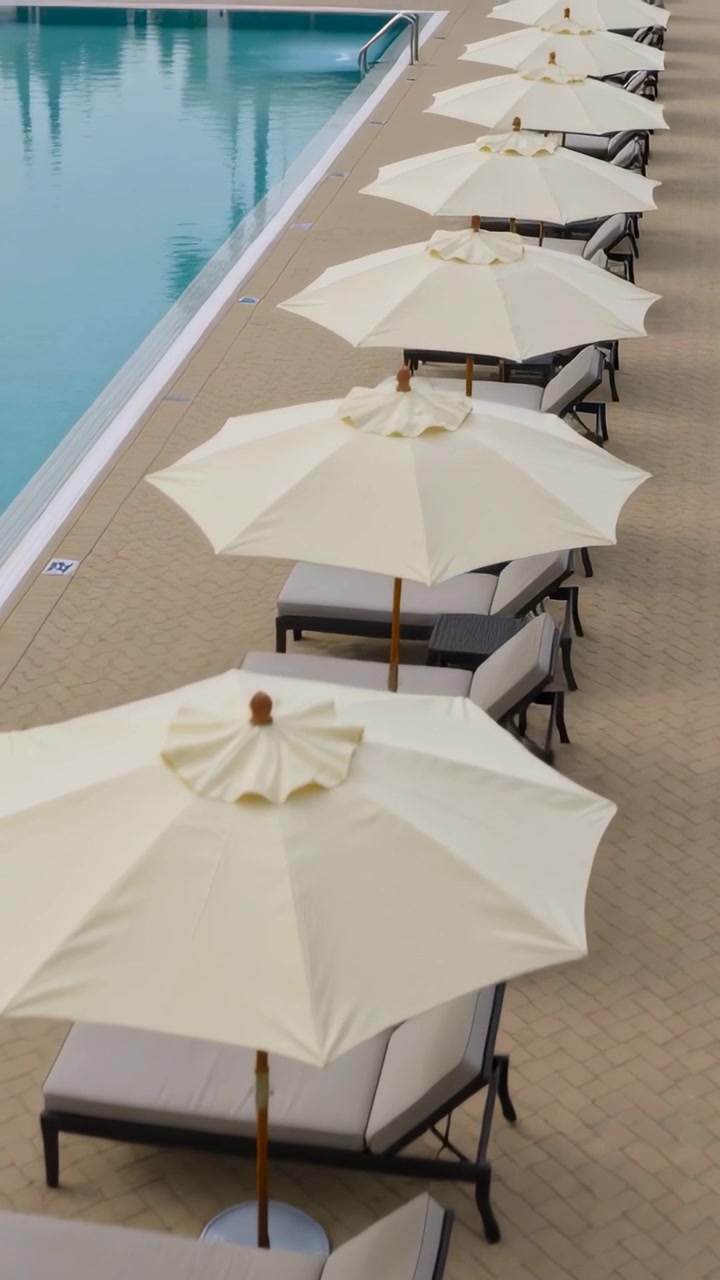 Vertical video: Panning camera starting near umbrella top, showing pool umbrellas and loungers