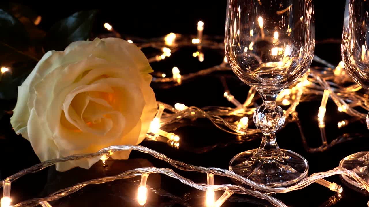 Calici da champagne e una rosa sullo sfondo di ghirlande luminose