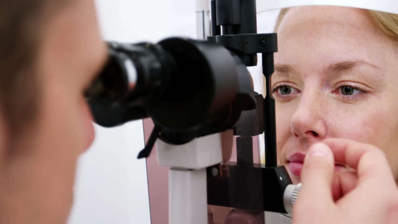 여성 환자 를 슬릿 램프 로 검사 하는 안경학자