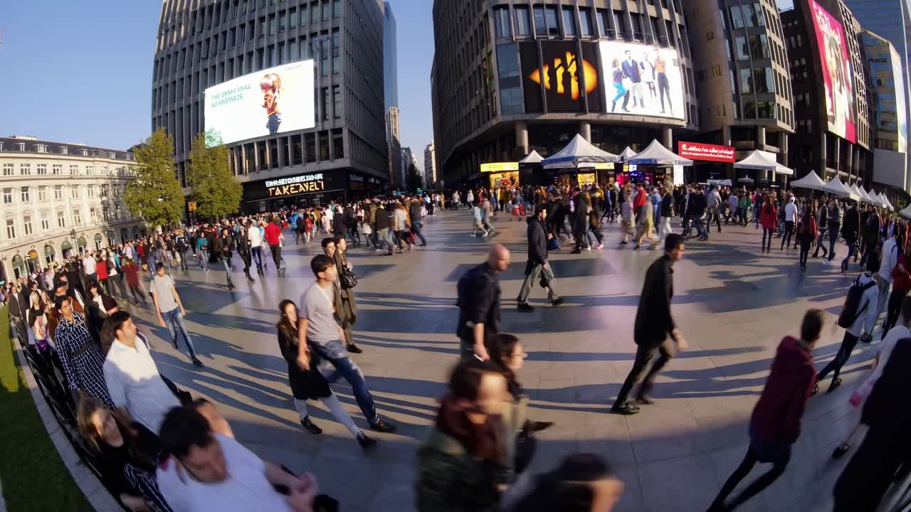 Wide-angle video shot captures a bustling urban plaza filled with people, showcasing dynamic city