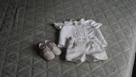 baby clothes and shoes neatly arranged on a quilted green bedspread