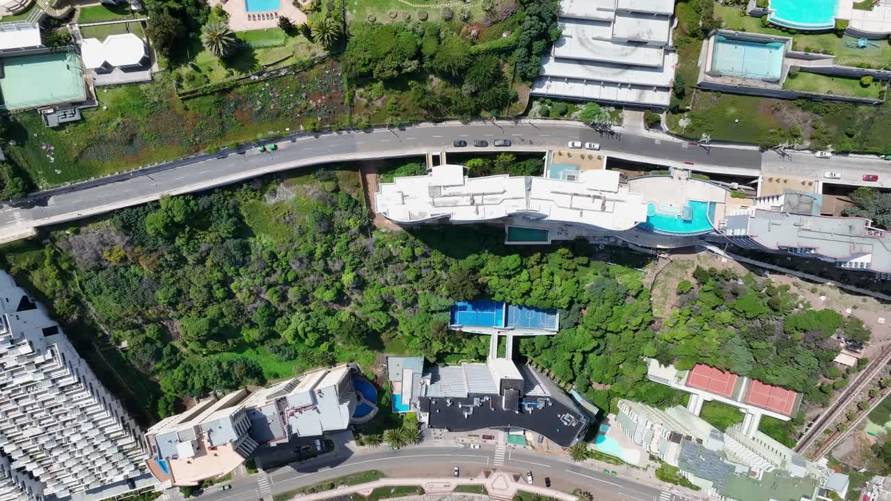 Forward top-down drone view of turquoise waves crashing on rocky coast, Viña del Mar, Chile with luxury villas, pools, and coastal promenade