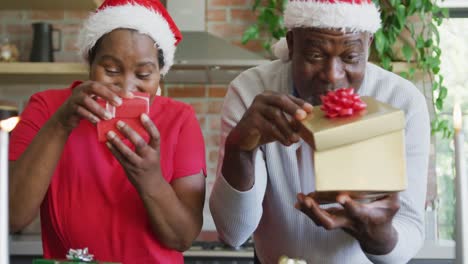 Happy-african-american-senior-couple-in-santa-hats-with-presents-on-video-call-at-christmas-time
