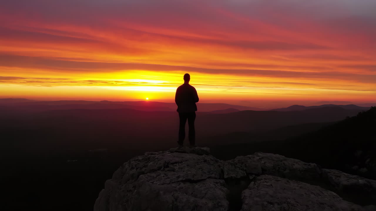 Silhouette of a person standing on a rock at sunset