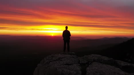 silhouette of a person standing on a rock at sunset