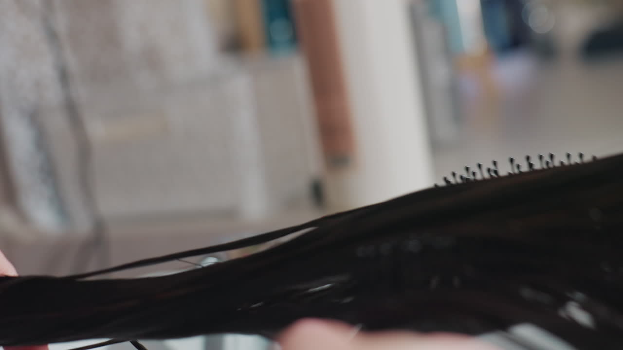 Profesional de la belleza alisando cabellos húmedos de forma profesional; estilista usando un cepillo de pala sobre mechones húmedos en un salón; peluquero arreglando cabello húmedo con un cepillo de pala dentro de un elegante salón.