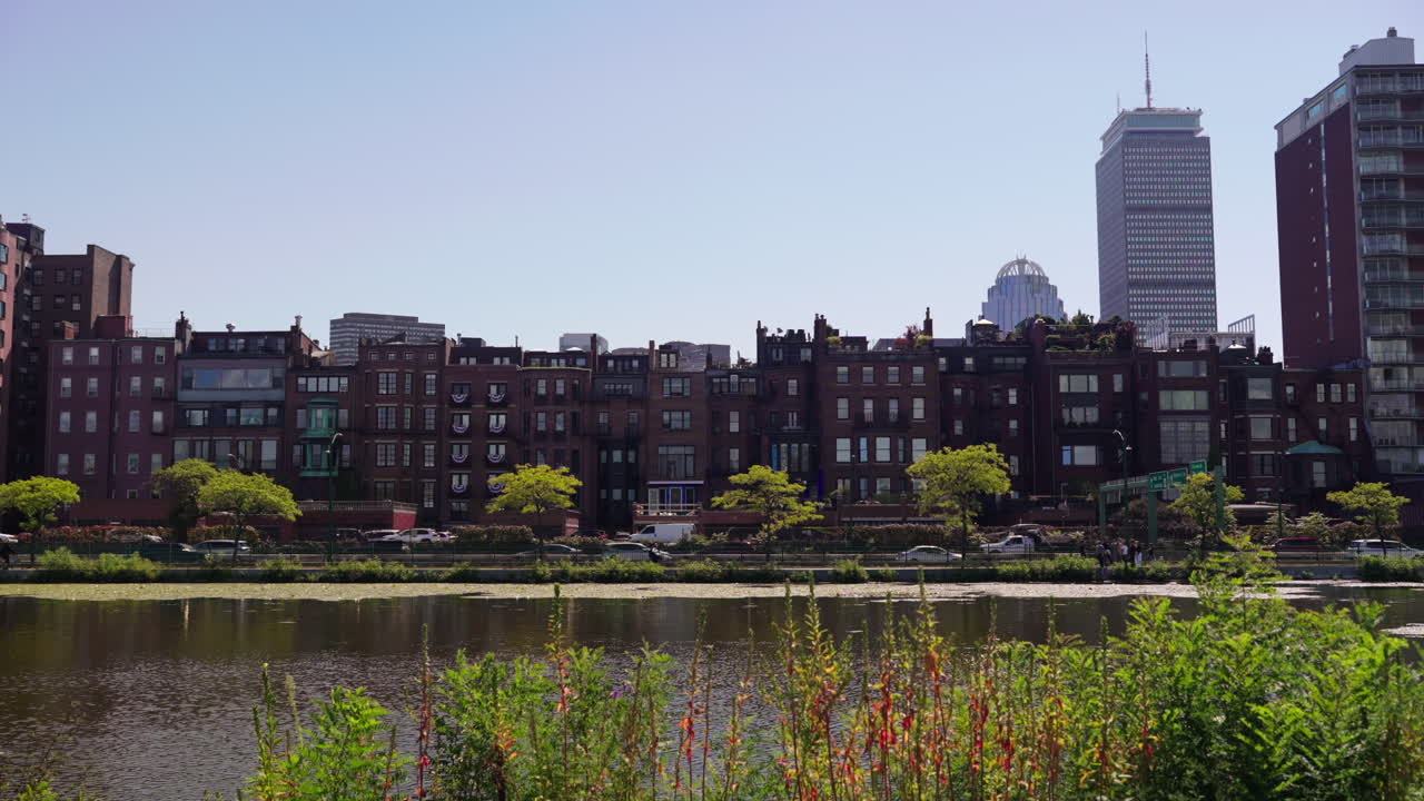 Static shot from across the Charles River showing colonial-style Boston buildings in front of modern skyscrapers on a sunny day