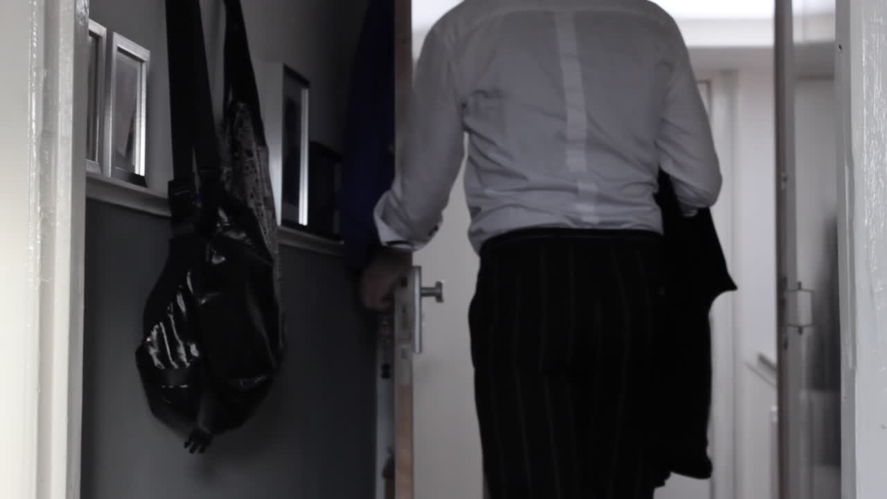 Back shot of a business man in a hallway grabbing his jacket and leaving his home