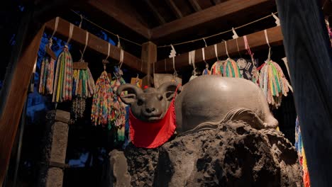 a shot of a stone ox statue located on the grounds of ushijima shrine. a red cloth is draped around its neck, and decorations resembling senbazuru (thousand paper cranes) are hung around it