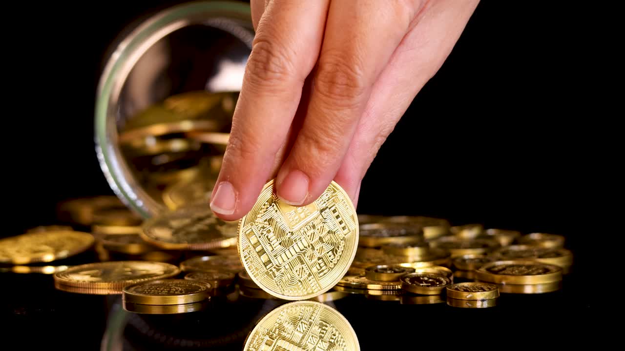 Hand spins gold coin on reflective surface near open jar of cryptocurrency tokens, dramatic lighting