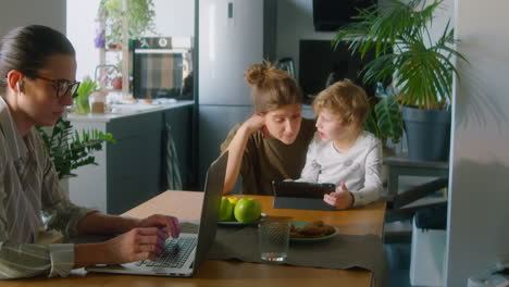 woman working on laptop while wife sitting with kid at home