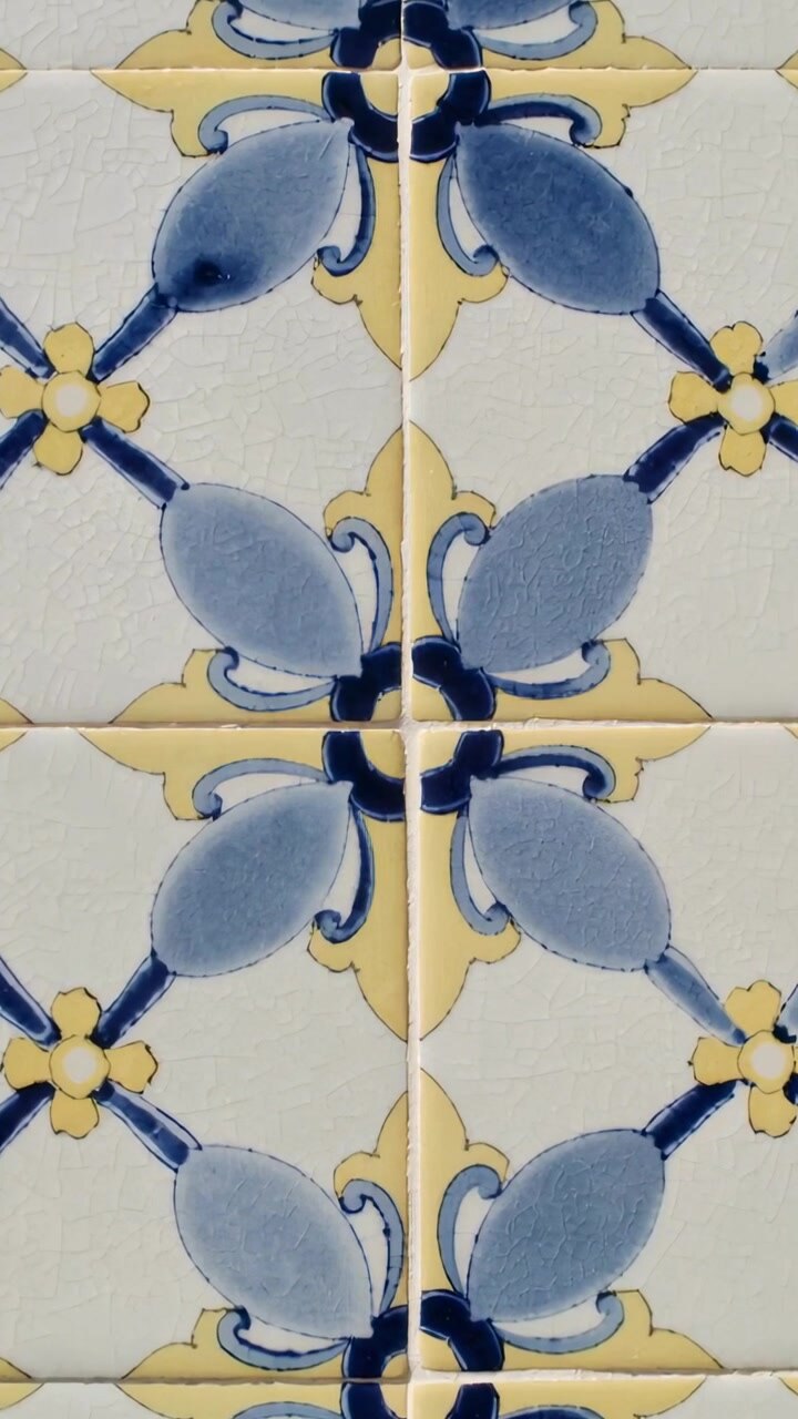 Vertical video: Panning camera down, revealing glazed ceramic tiles on wall with blue leaf motifs