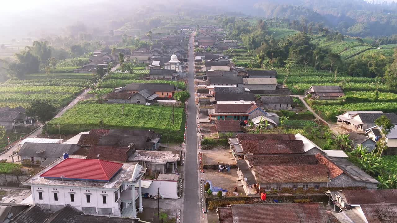 Drone capture of peaceful rural community surrounded by farmland with facing a misty mountain under the early morning sun. Village on the slope of Merapi volcanic mountain, Indonesia