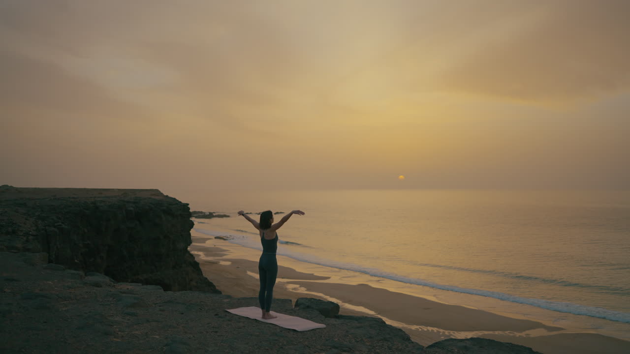 Woman practicing yoga at sunset on a coastal cliff
