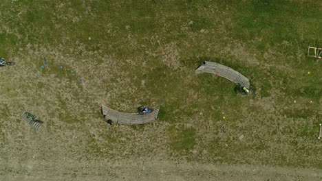 Top-down-aerial-of-mountainbikers-using-wooden-banked-turns-in-grass-field