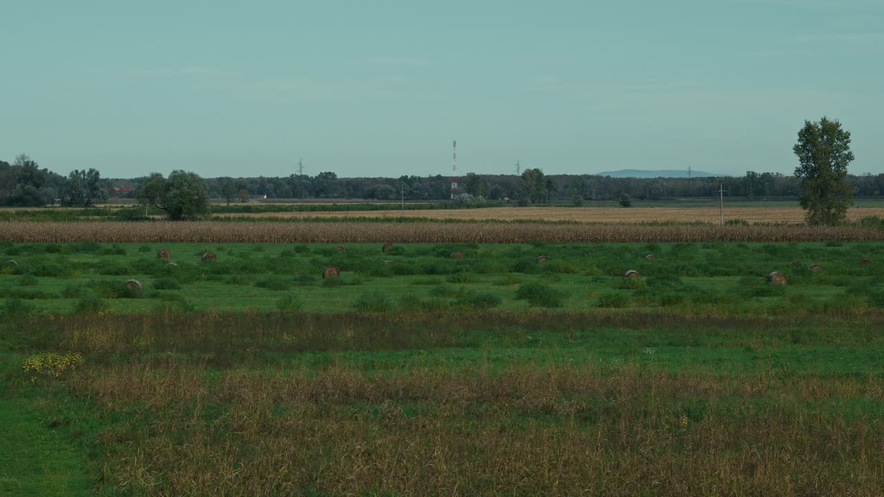 Expansive farmland with scattered hay bales, cornfields, and distant hills under a clear sky
