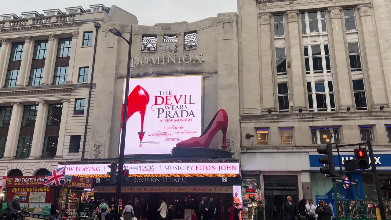 Handheld shot of Dominion Theatre exterior displaying new show: The Devil Wears Prada during a busy day in London.